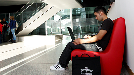 Student on laptop sat on red sofa