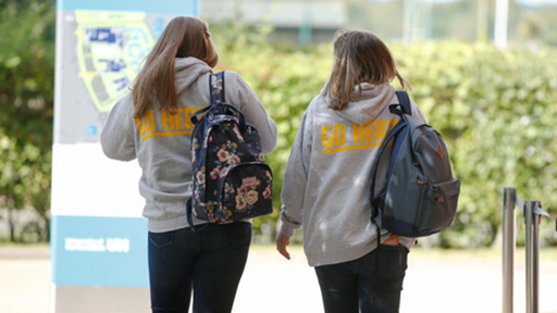 Two students in Go Herts hoodies walk on campus