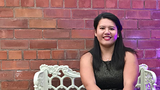 Michelle sits on a white cast iron bench, smiling to camera