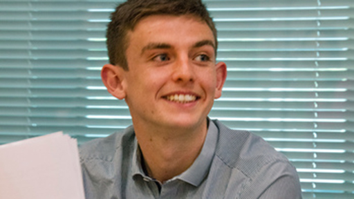 a male student holds papers and smiles